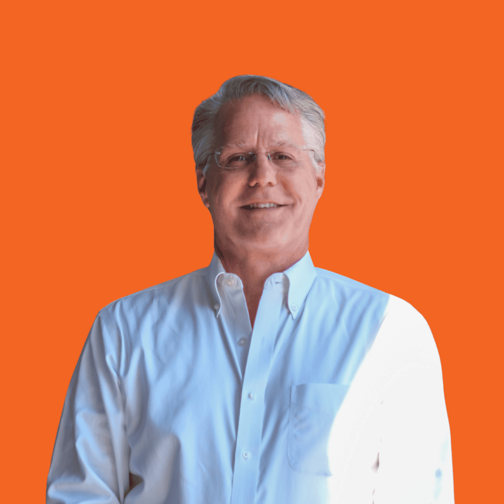 A smiling older man wearing glasses and a white button-down shirt stands against a bright orange background, with light casting a shadow on his right side.