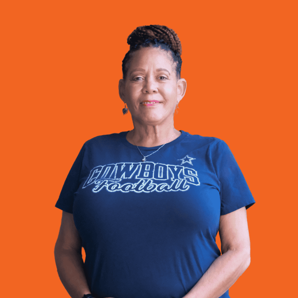 A woman with braided hair wears a navy blue Cowboys Football shirt, standing and smiling against a solid orange background.