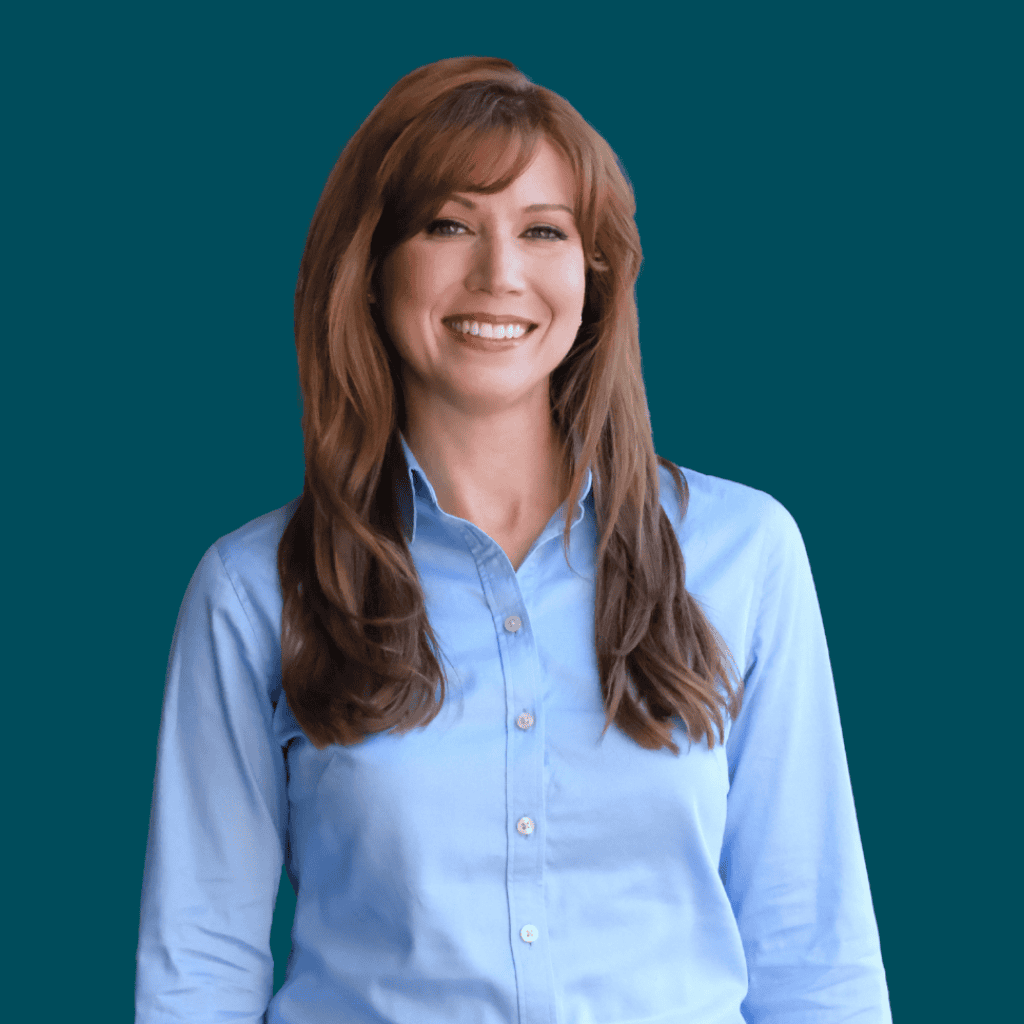 Smiling woman with long brown hair wearing a light blue button-down shirt, standing in front of a solid teal background.