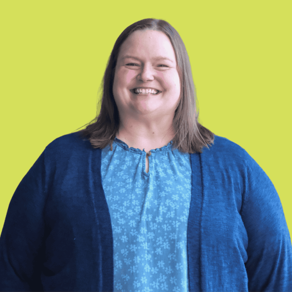 A woman with straight, shoulder-length brown hair smiles at the camera. She is wearing a blue patterned blouse and a dark blue cardigan. The background is a solid bright yellow-green color.