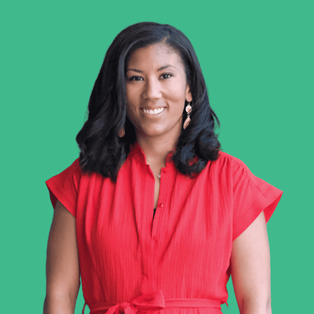 A woman with medium-length black hair wearing a bright red, short-sleeved dress stands smiling in front of a solid green background.