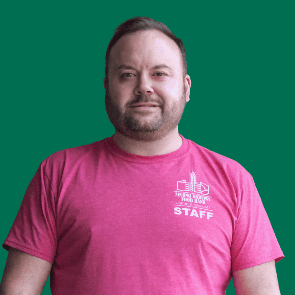 A person with short hair and a beard wearing a bright pink Second Harvest Food Bank STAFF t-shirt stands in front of a solid green background.