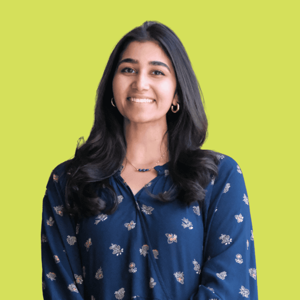 A woman with long dark hair wearing a blue floral blouse smiles at the camera, standing against a solid light green background.