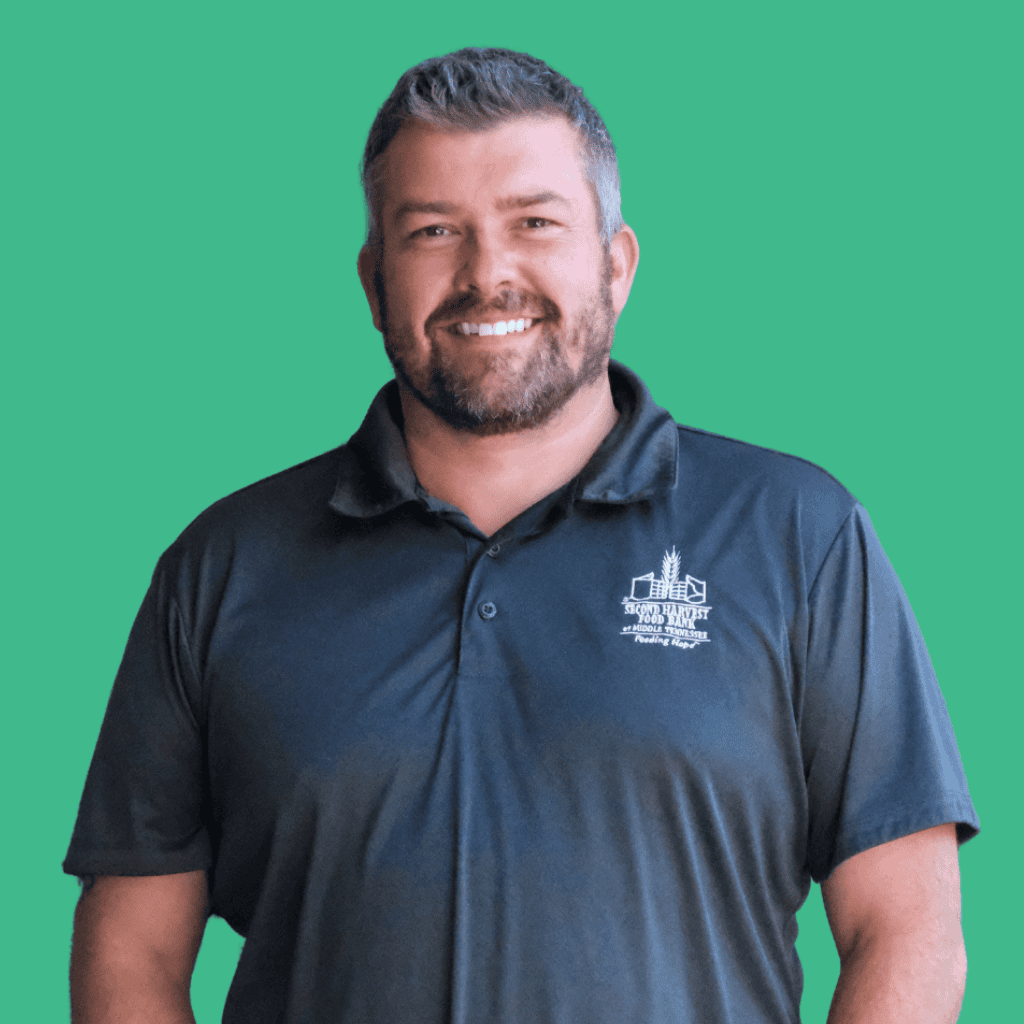 A smiling man with short gray hair and a beard wearing a dark polo shirt with a white building logo stands against a solid green background.