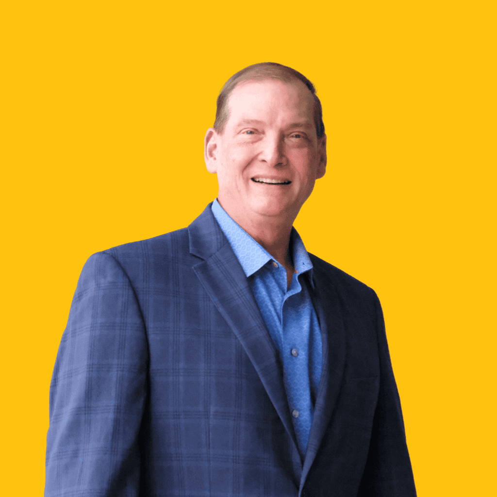 A smiling man in a blue checked suit jacket and light blue shirt stands in front of a solid yellow background.