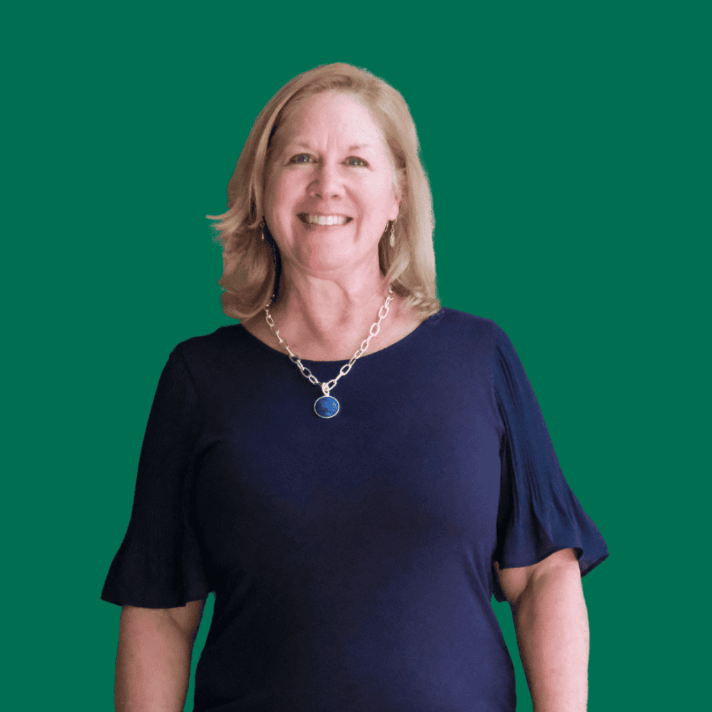 A smiling woman with shoulder-length blonde hair wearing a navy blue top and a silver necklace with a blue pendant, standing against a solid green background.