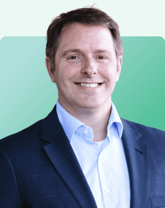 A man wearing a blue suit jacket and light blue dress shirt is smiling at the camera. The background is a gradient of light green to turquoise.