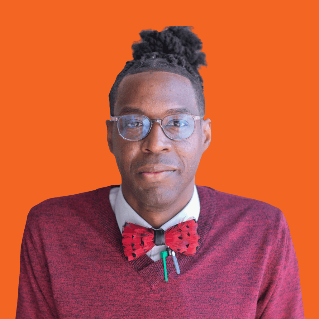 A person wearing glasses, a maroon sweater, white shirt, and a red bow tie with black details stands against an orange background. They have dark skin and their hair is styled in a high bun.