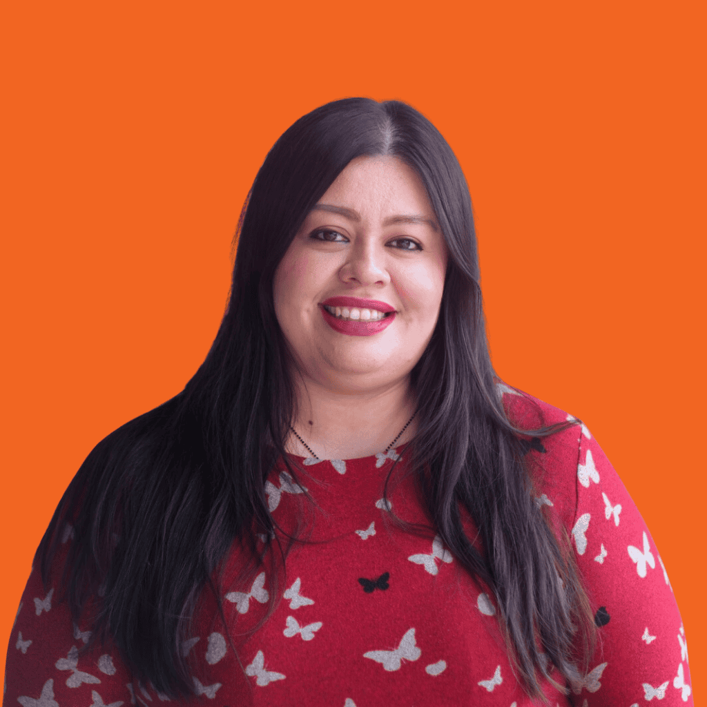 A woman with long dark hair smiles at the camera. She is wearing a red sweater with white and black butterfly patterns. The background is solid orange.