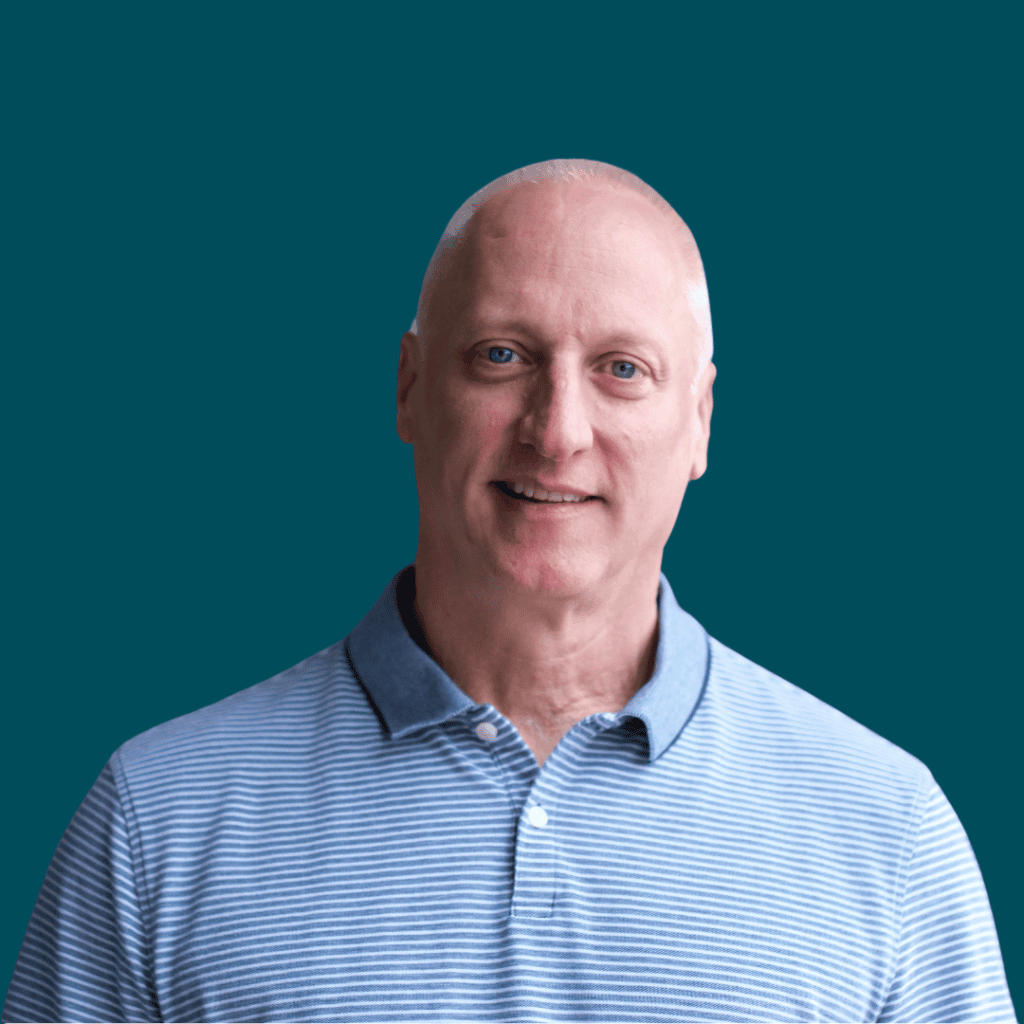 A middle-aged man with a shaved head wearing a light blue and white striped polo shirt, smiling and standing in front of a solid teal background.