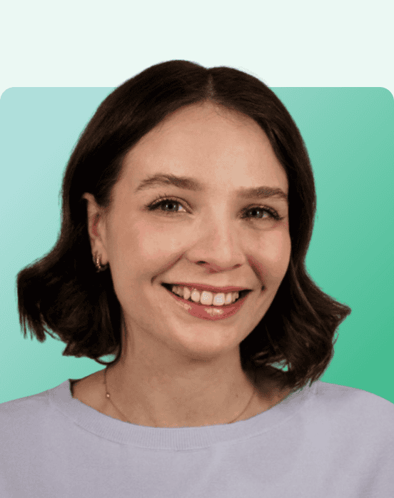 Smiling woman with short brown hair wearing a light purple top, gold earrings, and a necklace, posing in front of a green gradient background with rounded corners.